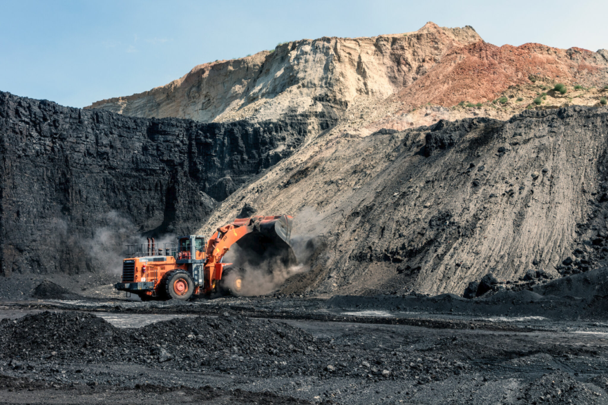 A construction vehicle inside an open-pit coal mine, which is visibly darker than the surrounding rocky areas.