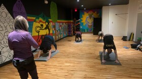 A woman stands in front of yoga students in downward dog.