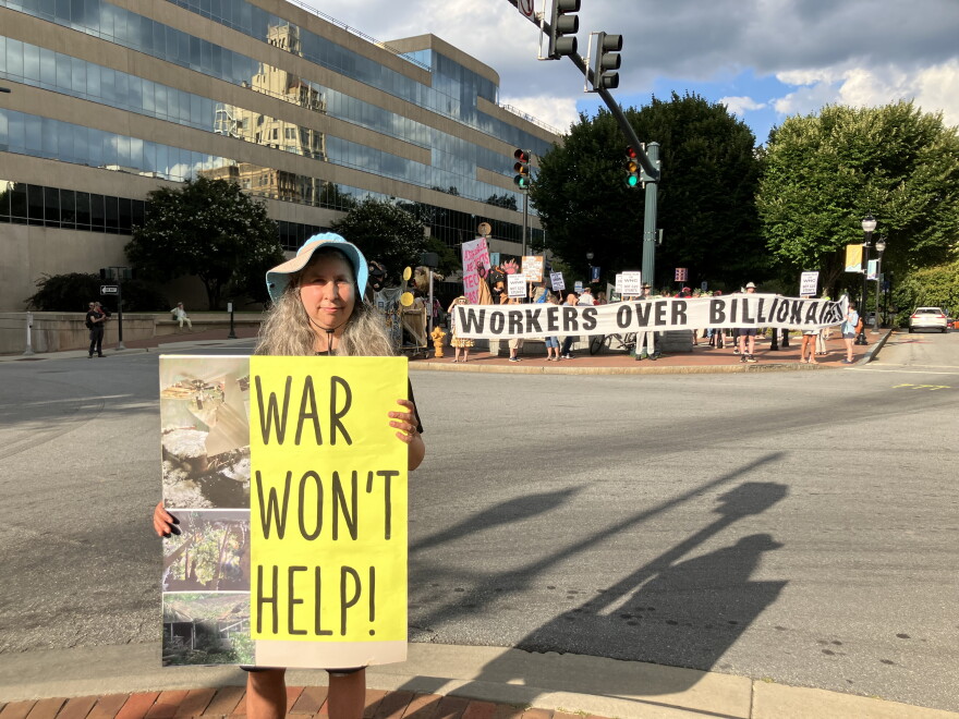 Demonstrator Lola La Fey holds a sign showing damage her home sustained from Hurricane Helene as she stands near Pack Square in Asheville on Friday, August 28, 2026.