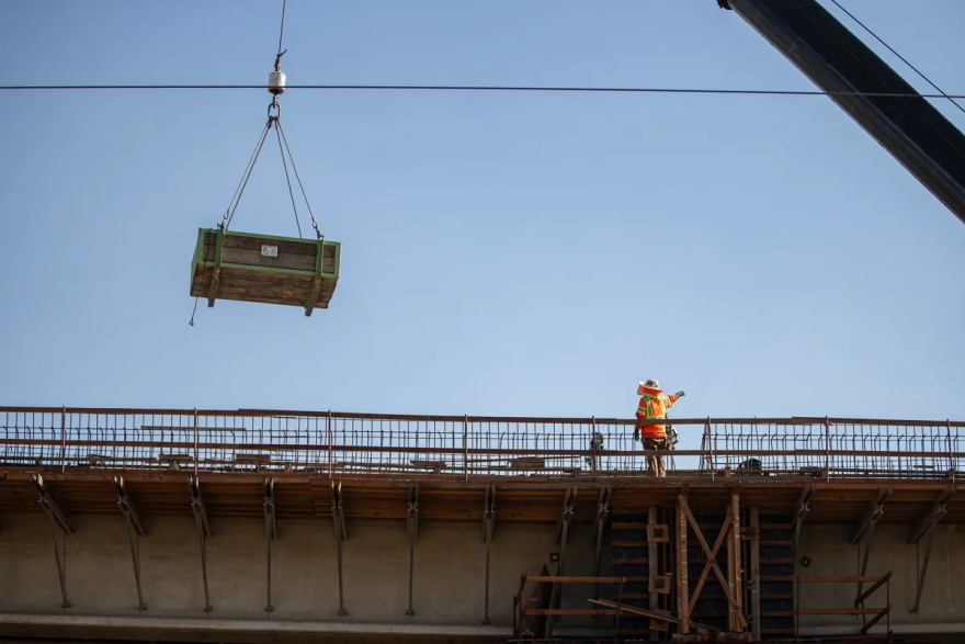 A worker guides a crane lifting material for construction on a segment of the high-speed rail.