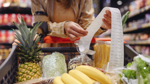 A person reads a receipt held over a cart of groceries.