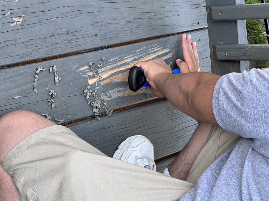 An incarcerated youth held at the Backbone Mountain Youth Center scrapes a deck as part of a community service project.