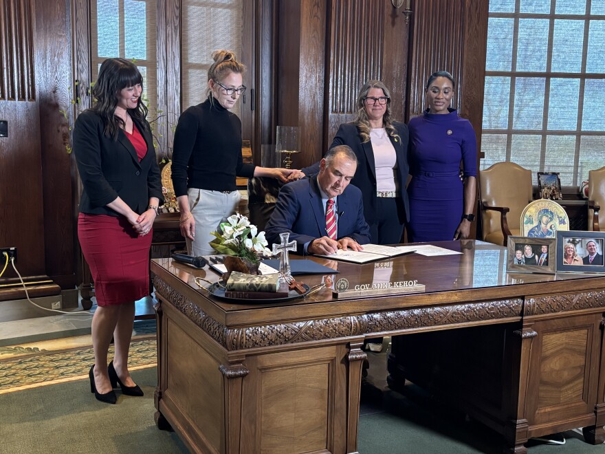 Gov. Mike Kehoe signs into law Tuesday legislation that removes legal barriers for pregnant women seeking divorce, while, from left, Rep. Ashley Aune, Sen. Jill Carter, Rep. Cecelie Williams and Rep. Raychel Proudie watch.