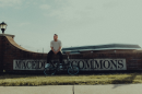 Brett Zupka sits on a brick wall with the Macedonia Commons sign on it