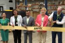 Five people stand behind a yellow ribbon while one of them cuts the ribbon with big scissors.