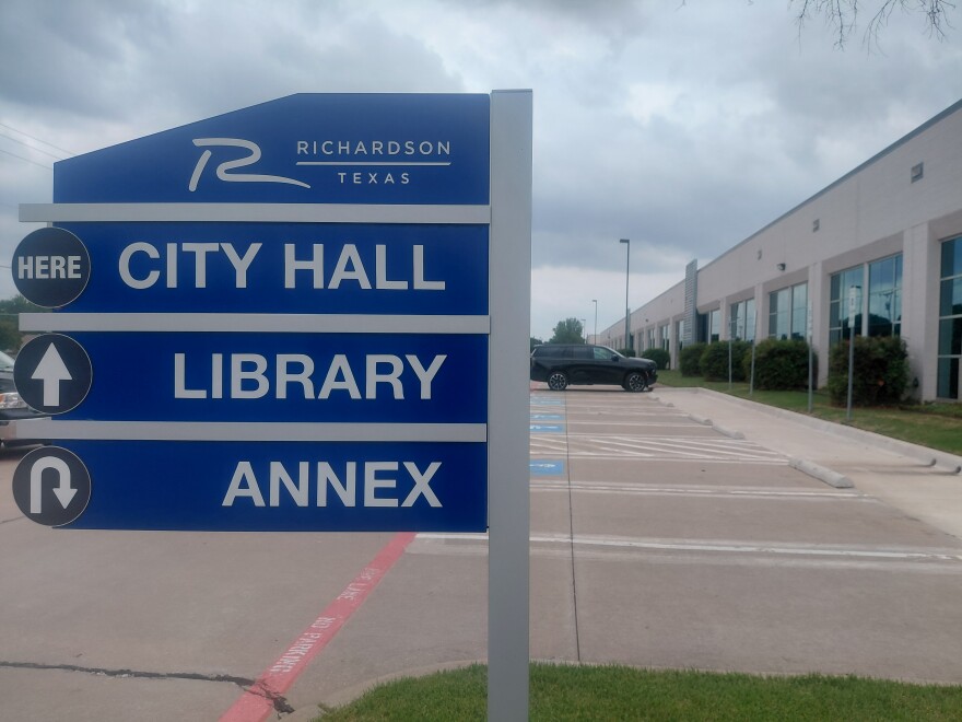 A blue sign in front of a municipal gray building reads Richardson City Hall, Library and Annex.