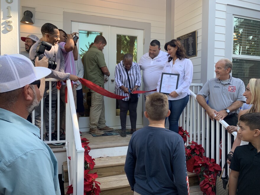 a woman cuts the ribbon a new home built for her by members of the community