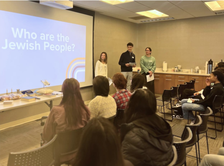 Three Jewish students speak in front of a classroom with a projection on the screen reading "who are the Jewish people?"