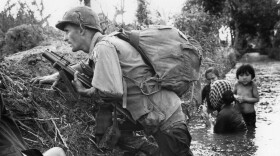 In this Jan. 1, 1966 file photo, a Paratrooper of the 173rd U.S. Airborne brigade crouches with women and children in a muddy canal as intense Viet Cong sniper fire temporarily pins down his unit during the Vietnamese War near Bao trai in Vietnam. (Horst Faas/AP)