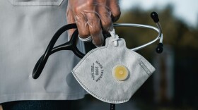 A person with a clear safety glove holds a stethoscope and a face mask.