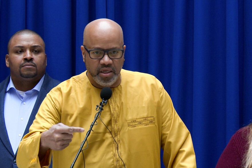 Rev. Ivan Hicks of the Indianapolis Ministerium stands in a yellow shirt behind a podium discussing a new Senate bill that would limit discussions on race within schools. 