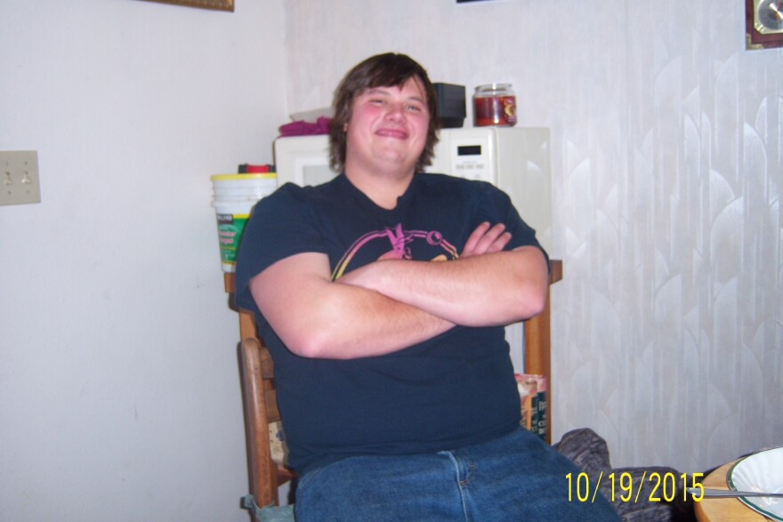 A smiling young man sits in a chair with his arms crossed.