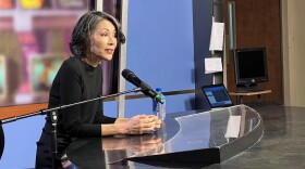 Journalist Ann Curry sitting behind a student anchor desk talking about reporting.