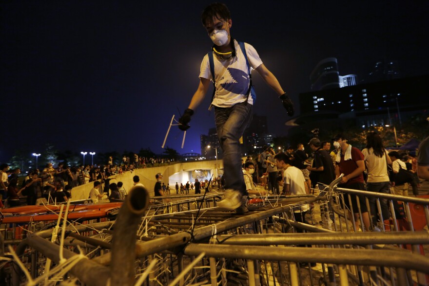 A demonstrator climbs over barriers as others block the main road with metal and plastic safety barriers outside government headquarters in Hong Kong's Admiralty district.