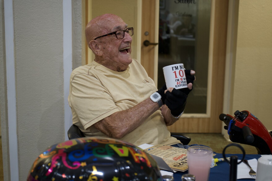 Michael Baker, World War II veteran of Ocala, smiles as he shows family and residents at Brookdale Senior Living a coffee mug gifted to him Thursday for his 101st birthday.