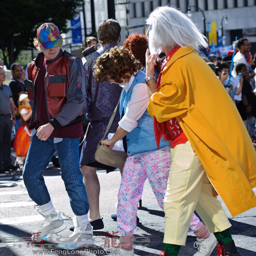 Three people, dressed as characters from the movie Back to the Future walk past a crowd of people.
