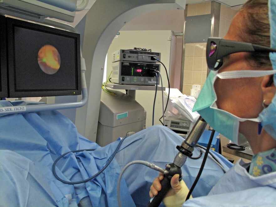 Dr. Dianne Sacco of Massachusetts General Hospital uses a laser ureteroscope to pulverize a kidney stone in Henry Owens. The screen shows a magnified image of the stone, an irregular yellow shape.