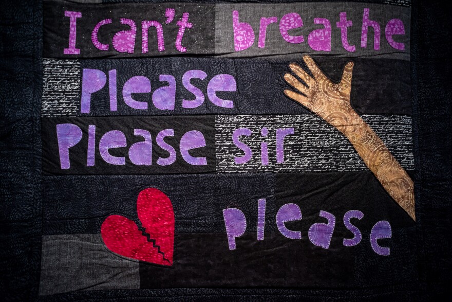A black fabric quilt is embroidered with the words, "I can't breathe. Please, sir, please."