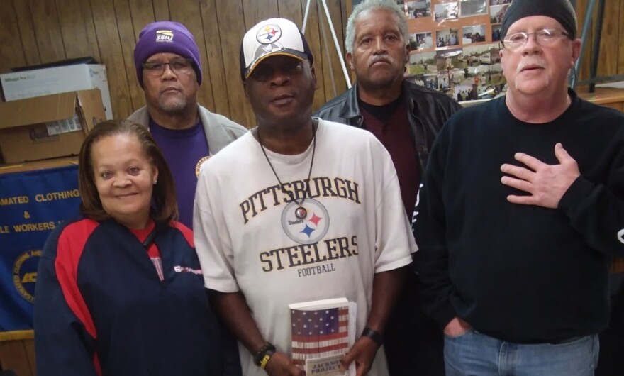 A group of five people standing together: one Black woman, three Black men and one white man.