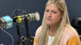 A woman sits inside a radio studio and is talking at a microphone.