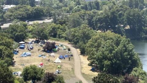 a view of tents in a clearing of trees near a river and road.