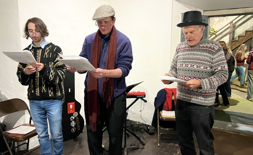 3 actors look down at their scripts while standing up. 