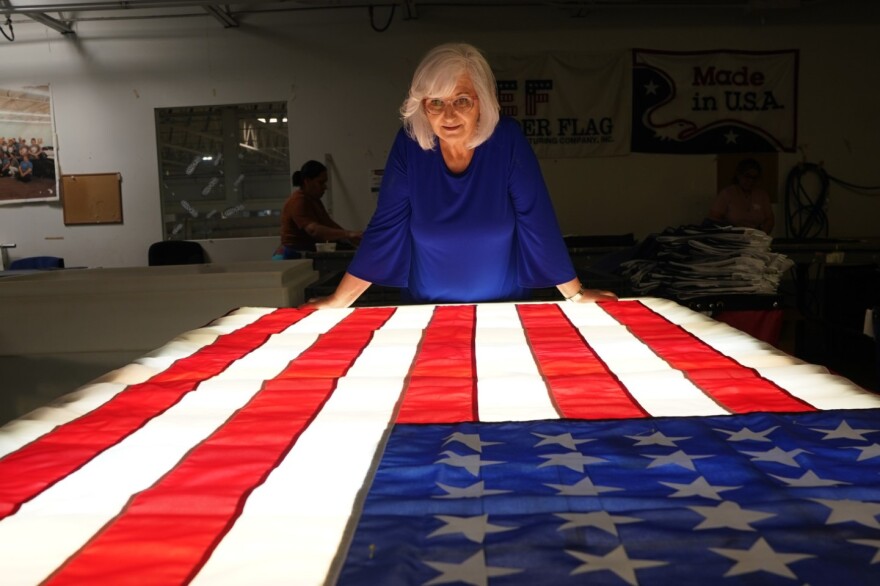 An elderly woman with white hair and glasses looks at an American flag illuminated from underneath by a light table.