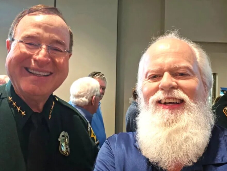 Male sheriff stands next to old man with white hair and long beard smiling for a selfie 