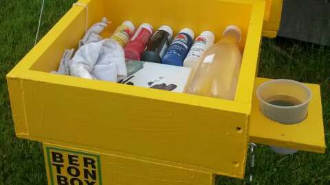 A yellow wooden box with paint supplies inside in a grassy outdoor setting