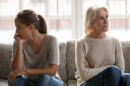In quarrel elderly mother grown up daughter sit on couch separately having conflict, intergenerational misunderstanding, adult grandchild grandma difficult bad relations different generations concept