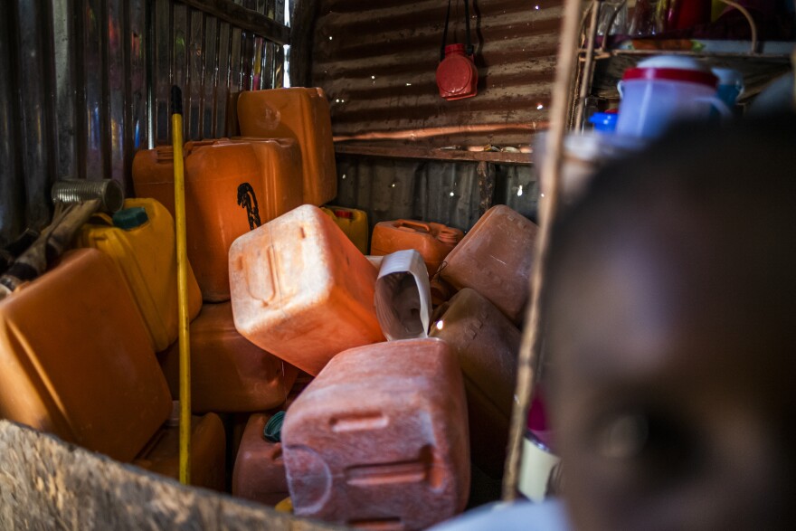 Empty jugs for water sit in a corner of Berthenid Dasny's home. Outside her door sits a large pile of stone and sand that she has been gradually purchasing in hopes of someday building a new home.