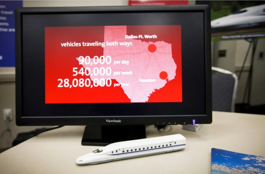 A computer monitor shows a graphic about the Dallas to Houston high-speed rail. A model of the train sits in front of the monitor.