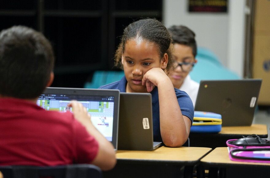 A young child sits by a computer in a classroom.