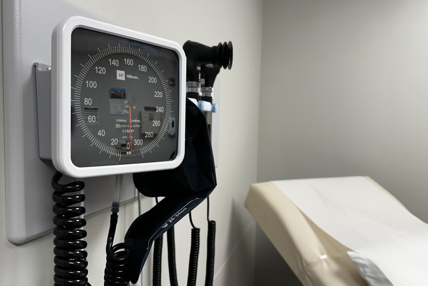 Medical instruments affixed to a wall in a medical exam room. An exam table is slightly blurred in the background.