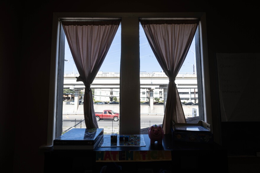 A view of I-35 from the second floor of Escuelita Del Alma. Curtains are tied in the window. The room is relatively dark.