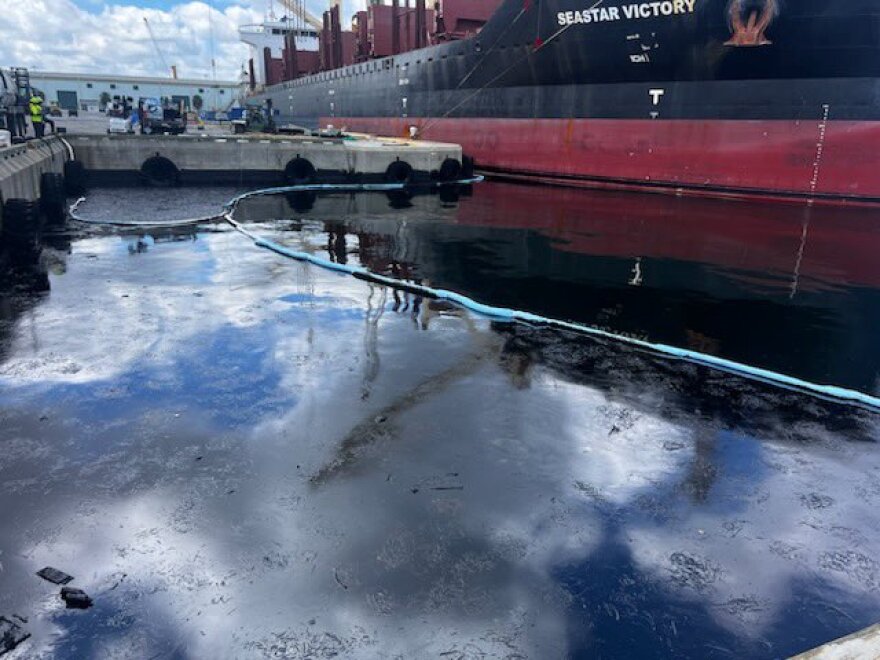 Oil spill in water between a dock and a large ship. 