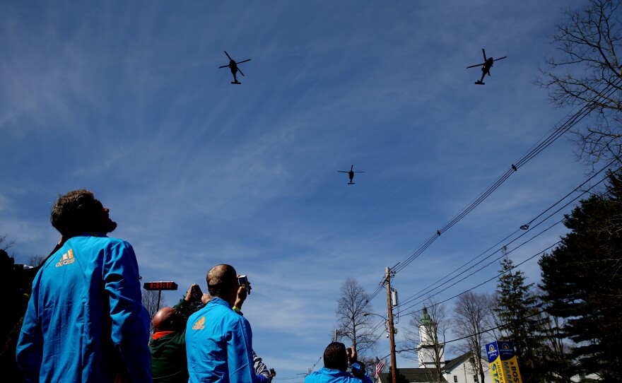 Volunteers look on during a flyover by the Massachusetts Army National Guard before the start of the marathon in Hopkinton.