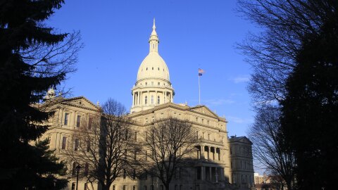 Winter three-quarter view of the state capitol building, lit by sunshine, framed by trees