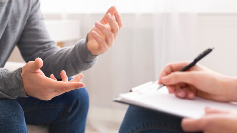 Psychotherapist writing notes, assessing patient's health and giving diagnosis to man sitting on couch during counseling session , panorama, free space.