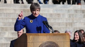 Kansas Governor Laura Kelly, draped in Democrat blue, speaks behind a wooden lectern at her second inauguration in 2023. 