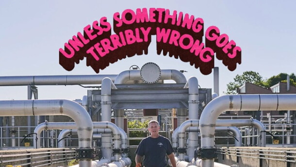 A man walking amid a series of large pipes in a sunny outdoor space; "Unless Something Goes Terribly Wrong" written in a pink arch overhead