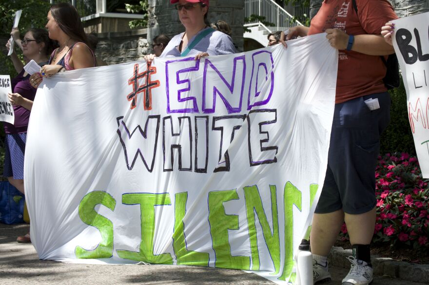 Event organizer Susan Prill holds a sign to Arts Fest patrons saying "#EndWhiteSilence."