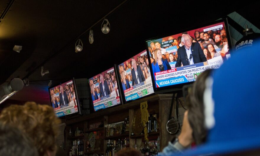 Television screens at a Las Vegas bar display Sanders speaking to a crowd, with the headline, "Breaking News: Sanders Addresses Supporters; CNN Projects He Wins Nevada."