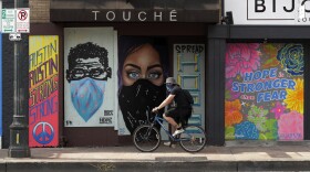 A cyclist wears a bandana over his face as he travels past a boarded up business in downtown Austin.