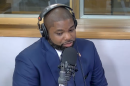 byron donalds speaks in a radio studio with a microphone in front. he is a black man wearing a blue suit