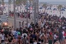 large group of people gathered on a beach sidewalk, water and sand in the background