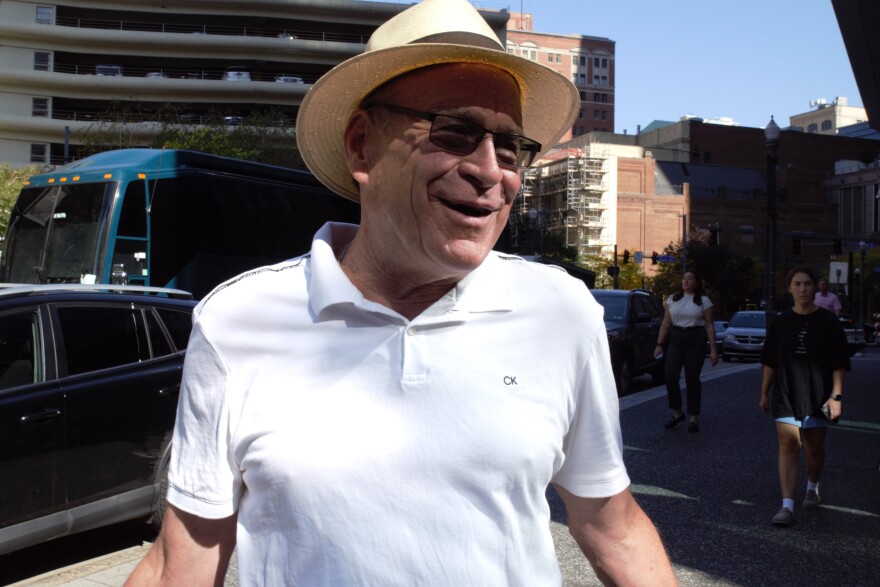 A man in a hat and sunglasses half-shrugs.