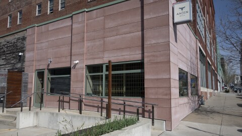Outdoor photo showing the exterior corner of a stone building. It has large, plate glass display windows. Some show kitchen items like a mixer and gourds in the display. Others allow a view into the restaurant. A small sign above reads "Anjin."