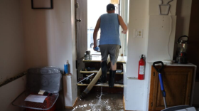 A man walks up a set of stairs as water pours into his home.