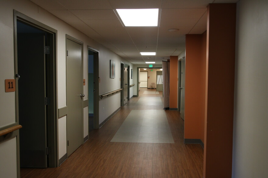 A long hallway with wooden floors. There are several rooms to the left and right. 